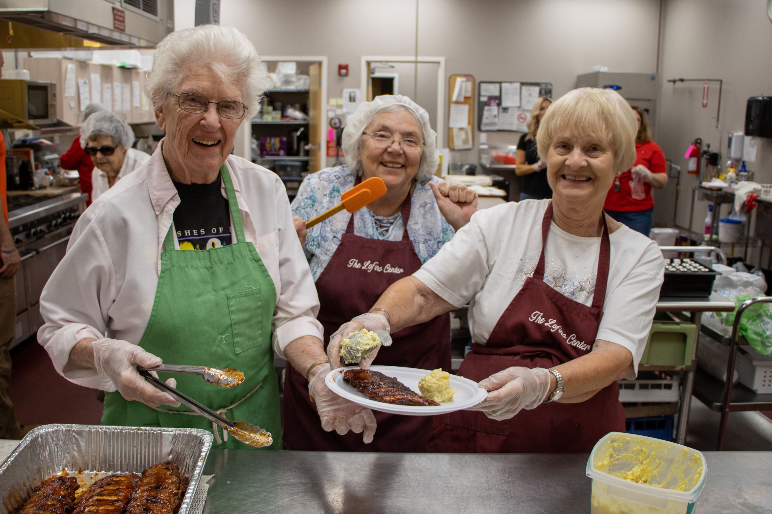 Three volunteer cooks smiling while plating food at the Beavercreek Senior Center 