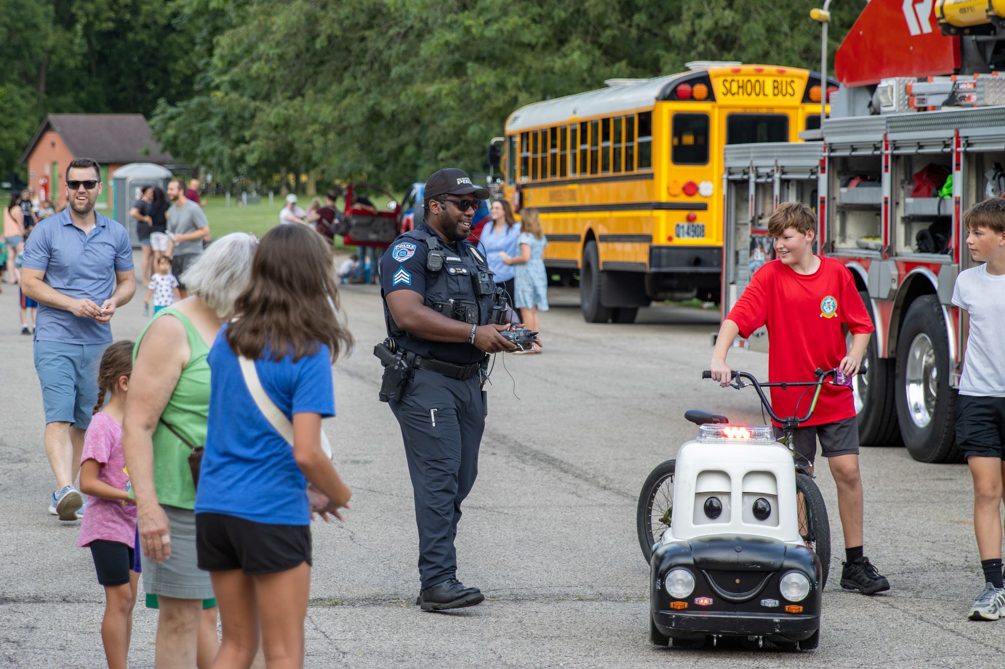 A police officer chats with kids while a boy pushes a small robot car at a safety event.