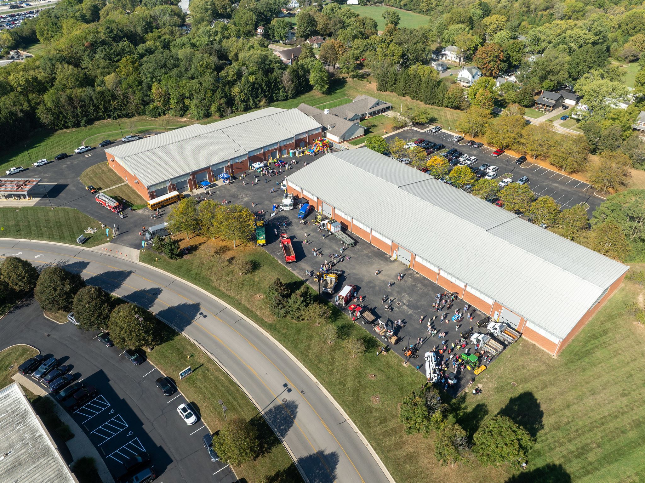 A drone view shows crowds exploring vehicles and activities outside large public works buildings.